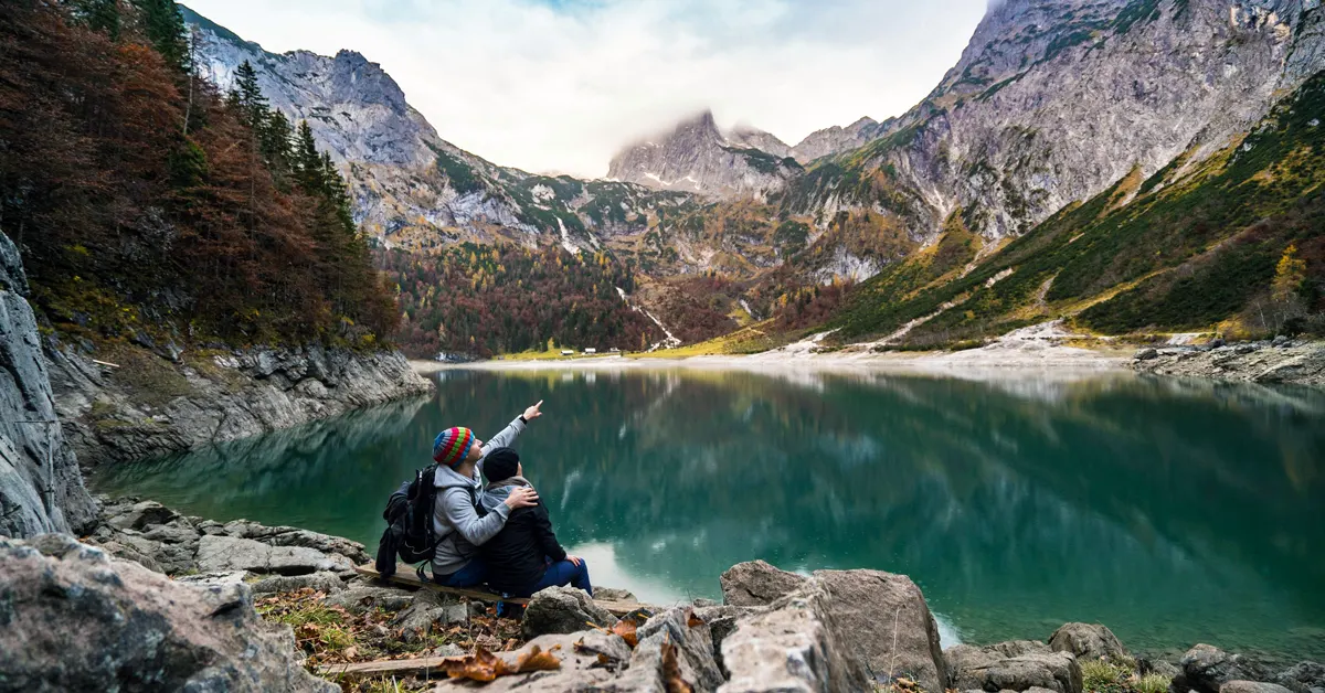A couple stands shoulder to shoulder in front of a  lake.