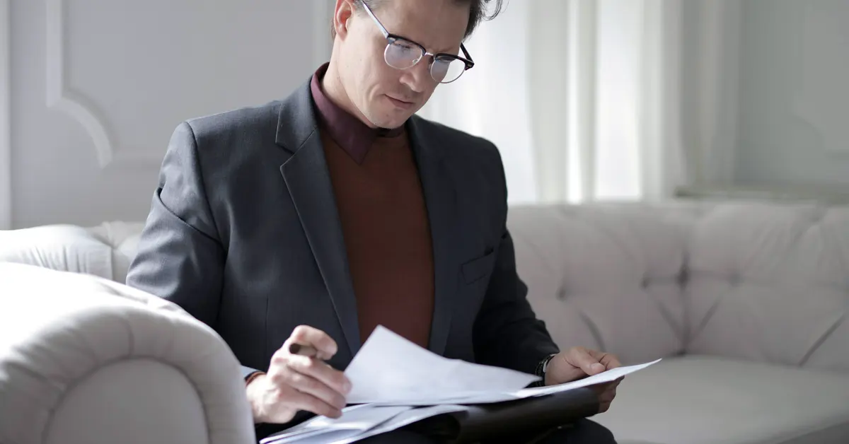 A hotel General Manager sits on a cream leather sofa, consulting documents.