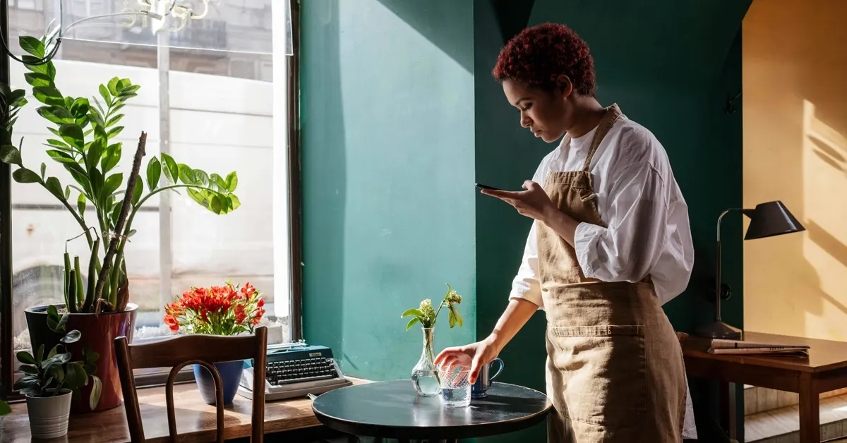 A young waitress standing in front of a table, placing a glass of water on it.