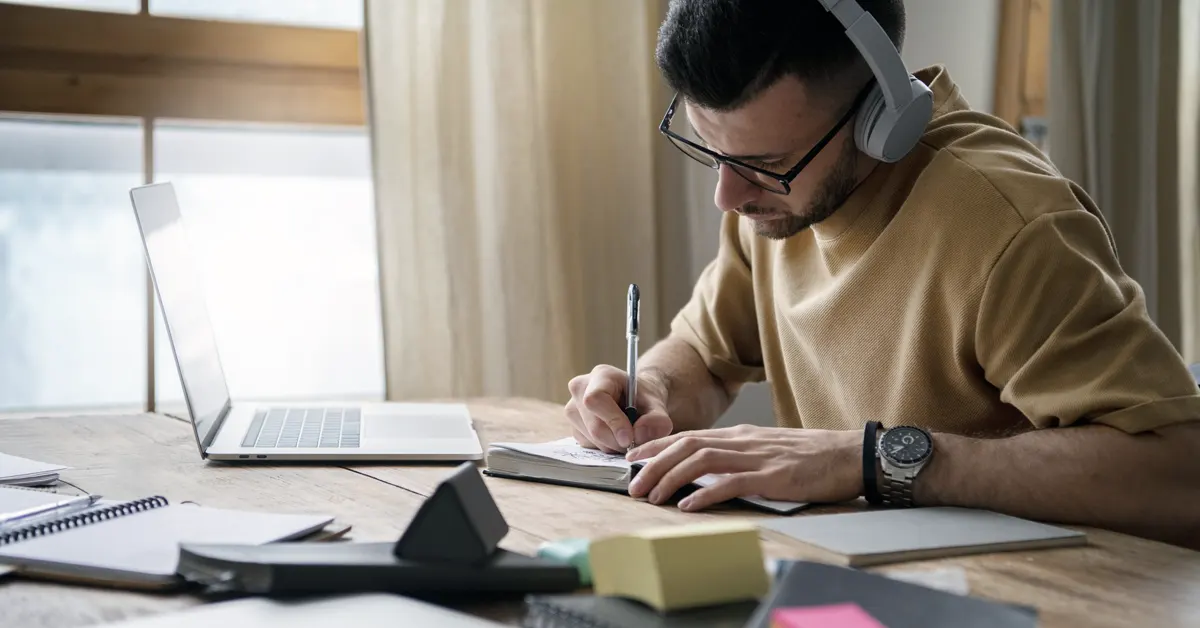 A man is focused intently on a book, a pen in hand as he studies.